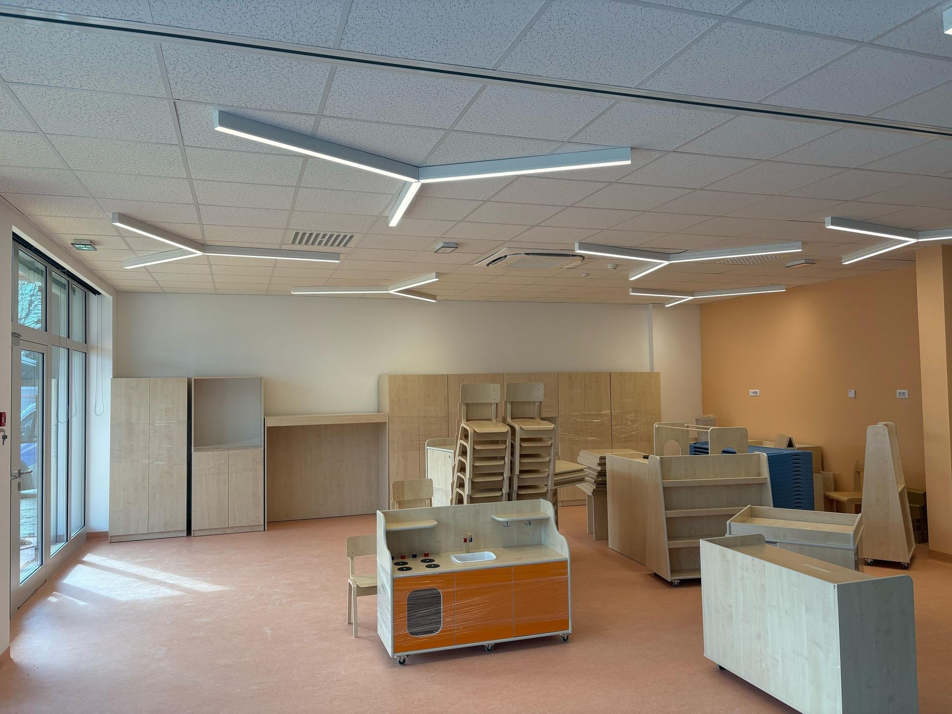 Empty classroom with modern wooden furniture, large windows, and unique ceiling lights.